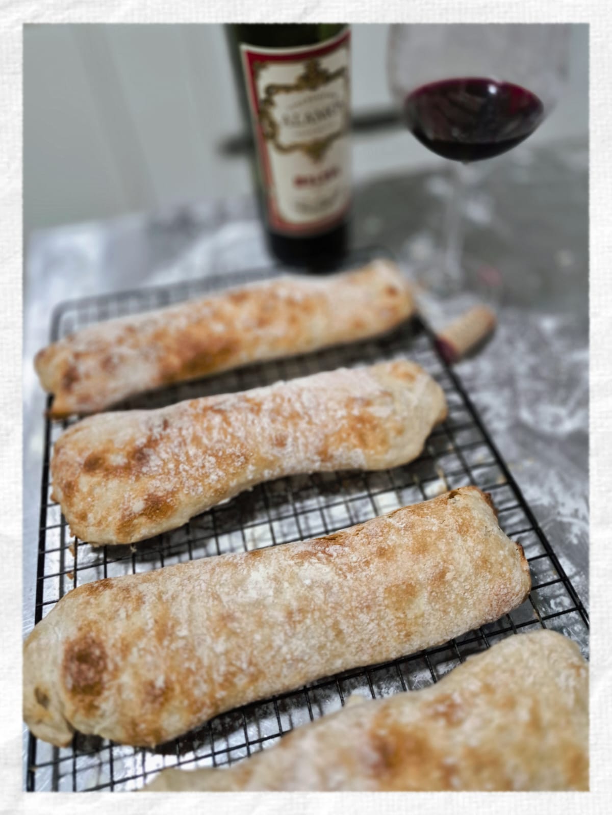 Três pães artesanais esfriando na grade ao lado de uma taça de vinho